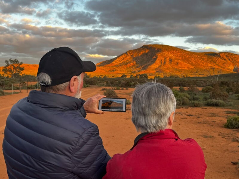 Sunset over the Australian Outback with two travelers capturing the scenic landscape.